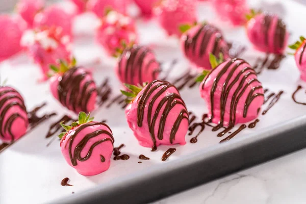 Decorating chocolate-covered strawberries with chocolate drizzles and sprinkles.