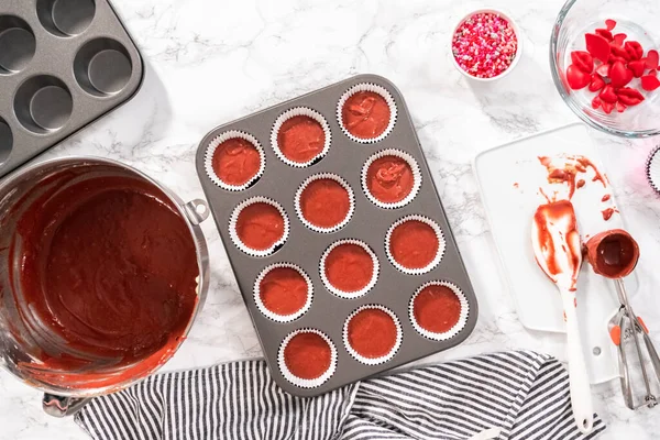 Flat lay. Flat lay. Scooping cupcake batter into a cupcake pan to bake red velvet cupcakes.
