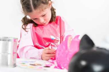 Küçük kız Cadılar Bayramı balkabağını akrilik boyayla boyuyor.