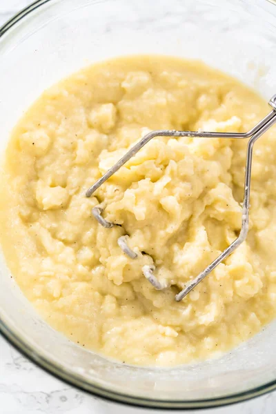 Mashed potatoes. Mashing cooked potatoes in a glass mixing bowl with a potato masher to make mashed potatoes.