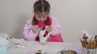 COVID-19 tecridi sırasında evde eğitim. Küçük kız kağıt mache dinozor heykelciğini akrilik boyayla boyuyor..