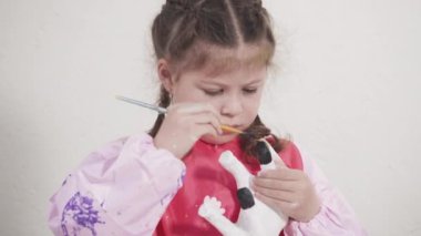 COVID-19 tecridi sırasında evde eğitim. Küçük kız kağıt mache dinozor heykelciğini akrilik boyayla boyuyor..