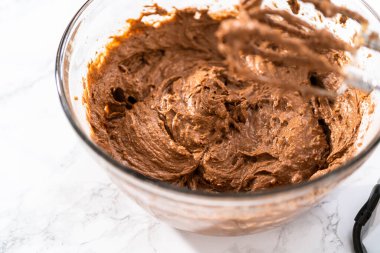 Büyük bir bardakta ıslak malzemeler karıştırarak kırmızı kadife kekler ve beyaz çikolatalı ganache kreması pişiriyorum..