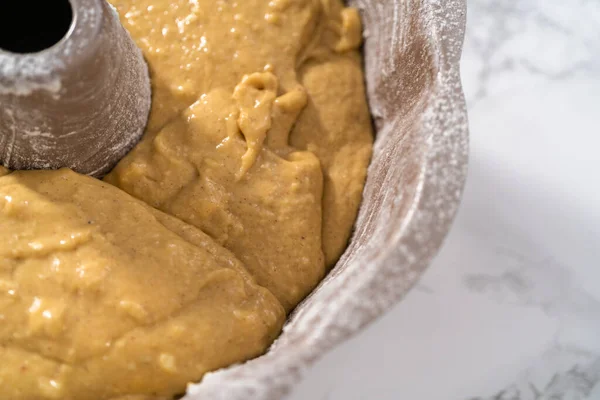 Filling metal bundt cake pan with cake butter to bake eggnog bundt cake with an eggnog glaze.