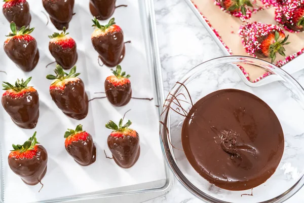Preparing chocolate covered strawberries on a cookie tray.