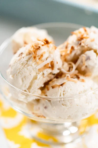 Homemade coconut ice cream garnished with roasted coconut flakes in a glass ice cream bowl.