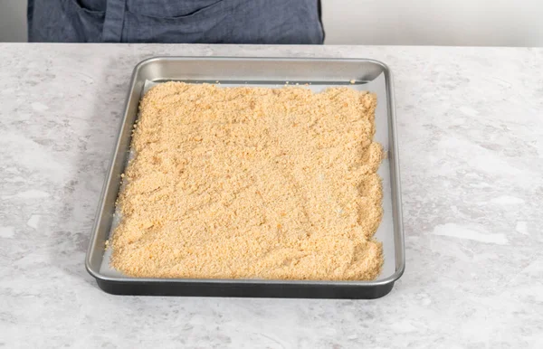 Spreading bread crumbs on a baking sheet lined with parchment paper to prepare dried bread crumbs.
