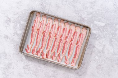 Flat lay. Uncooked bacon strips on a baking sheet with white parchment paper.