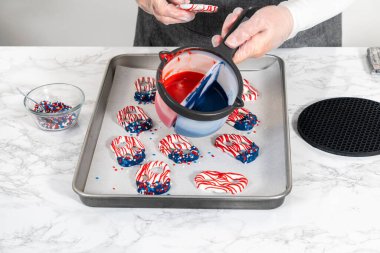 Flat lay. Dipping pretzels twists into melted chocolate to make red, white, and blue chocolate-covered pretzel twists.