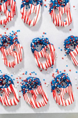 Dipping pretzels twists into melted chocolate to make red, white, and blue chocolate-covered pretzel twists.