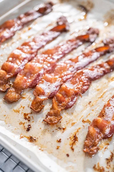 Cooked bacon strips on a baking sheet with white parchment paper.