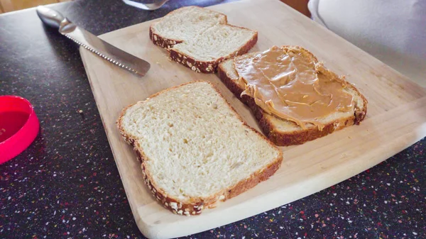 Preparing peanut butter and jelly sandwich on a wood cutting board.