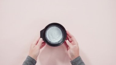 Siyah plastik bir kasede pembe arka planda saç boyası tozu..