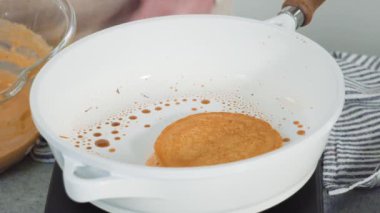 Time lapse. Step by step. Frying pumpkin pancakes batter on a white frying pan.