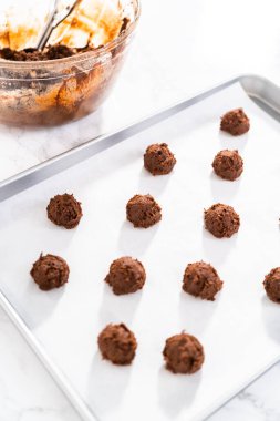 Scooping cookie dough with dough scoop into a baking sheet lined with parchment paper to bake chocolate cookies with chocolate hearts for Valentines Day.