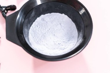 Siyah plastik bir kasede pembe arka planda saç boyası tozu..