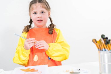 Evde akrilik boyalı bir sanat projesi üzerinde çalışan küçük bir kız..