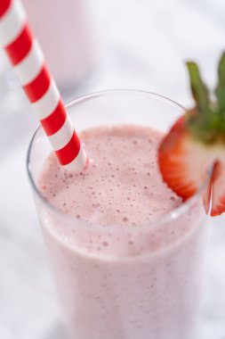 Taze taze çilek ve kağıt kamışla süslenmiş sağlıklı bir kahvaltı muzlu smoothie..