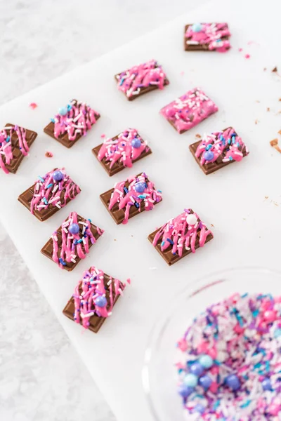 Drizzling melted pink chocolate on top of the mini chocolates and sprinkling some colorful sprinkles on top.