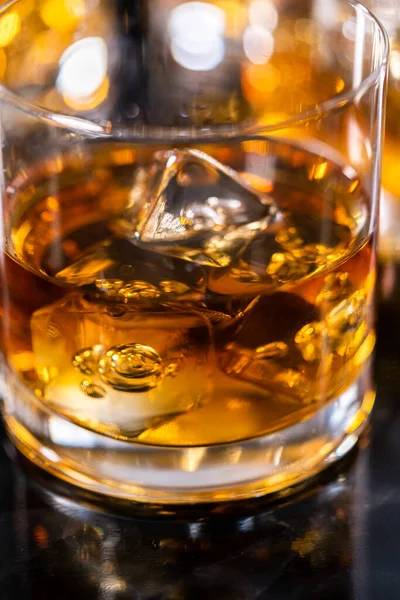 Scotch on the rocks in whiskey glass on a black marble surface.
