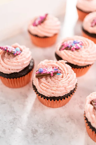 Packaging freshly baked chocolate strawberry cupcakes garnished with gourmet mini pink chocolates into a white paper cupcake box.