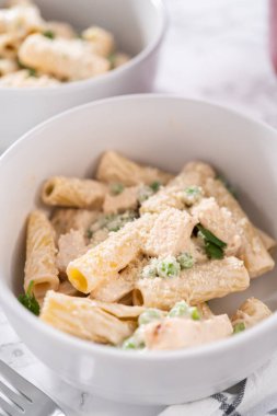 Küçük bir kasede yeşil bezelyeli tavuk ve rigatoni makarna..