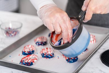 Dipping pretzels twists into melted chocolate to make red, white, and blue chocolate-covered pretzel twists.