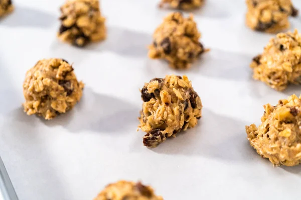 Scooping cookie dough with dough scoop into a baking sheet lined with parchment paper to bake soft oatmeal raisin walnut cookies.