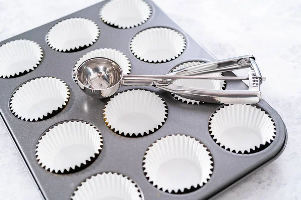 Lining cupcake baking pan with foil cupcake liners to bake unicorn rainbow chocolate cupcakes.