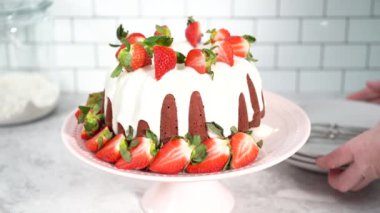 Step by step. Slicing red velvet bundt cake with cream cheese frosting garnished with fresh strawberries.