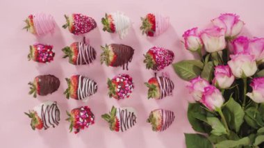 Flat lay. Variety of chocolate dipped strawberries with bouquet of roses on a pink background.
