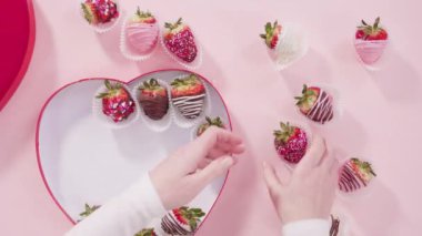 Zaman aşımı. Düz yatıyordu. Adım adım. Pembe arka planda kalp şeklinde bir hediye kutusuna çeşitli çikolata soslu çilekler yerleştirmek..