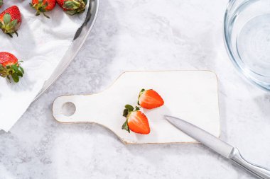 Beyaz bir kesme tahtasının üzerinde taze organik çilek dilimliyorum..