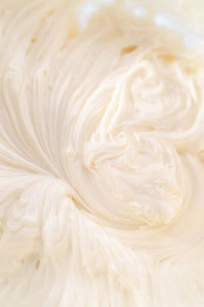 Mixing ingredients in a large glass mixing bowl to prepare cream cheese frosting.