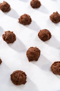 Scooping cookie dough with dough scoop into a baking sheet lined with parchment paper to bake chocolate cookies with chocolate hearts for Valentines Day.