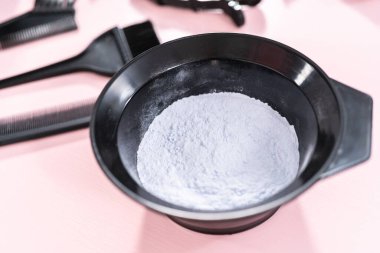 Siyah plastik bir kasede pembe arka planda saç boyası tozu..