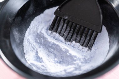 Siyah plastik bir kasede pembe arka planda saç boyası tozu..