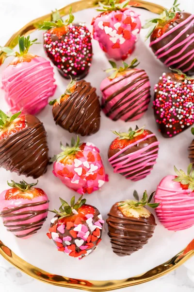 Gourmet chocolate-covered strawberries decorated with chocolate drizzles and sprinkles on a white plate.