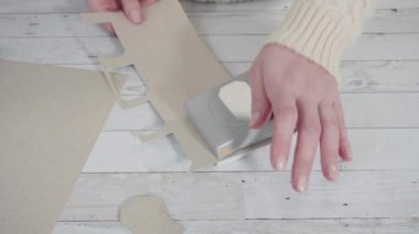 Adım adım. Kahverengi kağıttan hediye etiketlerini kağıt punçla kesiyor..