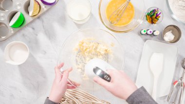 Düz yatıyordu. Adım adım. Vanilyalı Mardi Gras kekleri pişirmek için karışımı elektrikli mikserle karıştırıyorum..