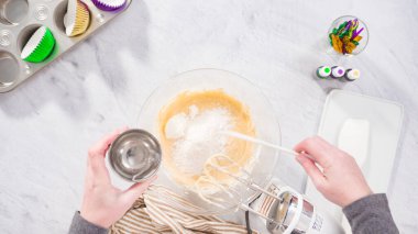 Düz yatıyordu. Adım adım. Vanilyalı Mardi Gras kekleri pişirmek için karışımı elektrikli mikserle karıştırıyorum..