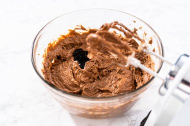 Büyük bir bardakta ıslak malzemeler karıştırarak kırmızı kadife kekler ve beyaz çikolatalı ganache kreması pişiriyorum..