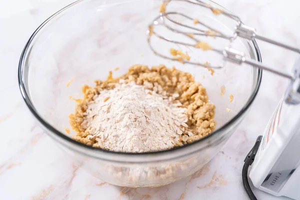 Mixing ingredients in a large glass mixing bowl to bake apple oatmeal cookies.