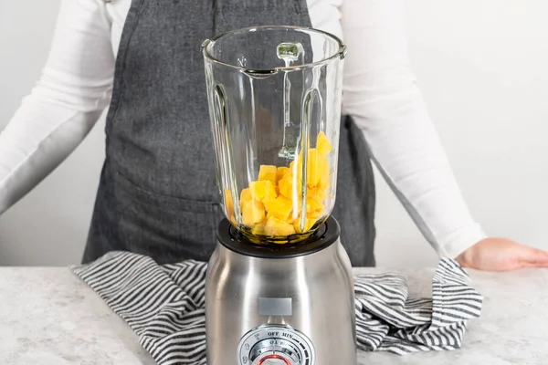 Mixing ingredients in kitchen blender to prepare mango boba smoothie.