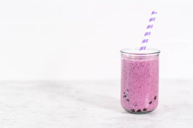 Freshly made mixed berry boba smoothie in a drinking jar with paper straw.