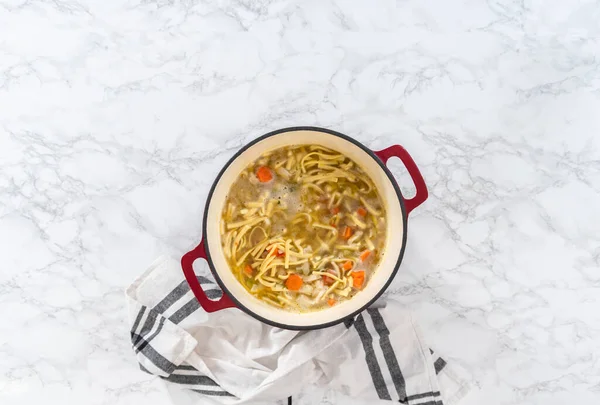Flat lay. Cooking chicken noodle soup with kluski noodles in an enameled dutch oven.