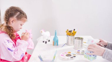 Küçük kız evde eğitim projesi için akrilik boyayla heykelcikler boyuyor..