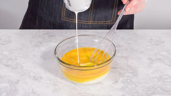 Step by step. Mixing ingredients in a glass mixing bowl to prepare coconut banana pancakes.