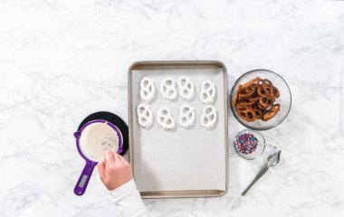 Flat lay. Dipping pretzels twists into melted chocolate to make red, white, and blue chocolate-covered pretzel twists.
