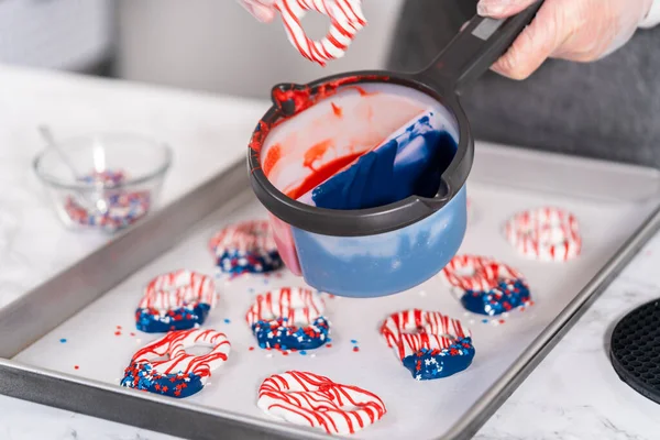 Dipping pretzels twists into melted chocolate to make red, white, and blue chocolate-covered pretzel twists.